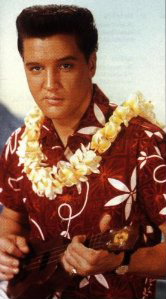 The famous photo from the movie Blue Hawaii with Elvis in an Hawaiian shirt and lei playing a ukulele 