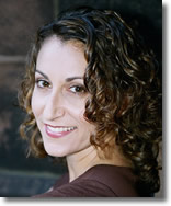 White woman with curly brown hair smiling over her shoulder at the camera
