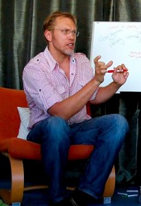 Sex and relationship expert Reid Mihalko of ReidAboutSex.com wearing a red and white checkered shirt writing on a white board on his lap while teaching