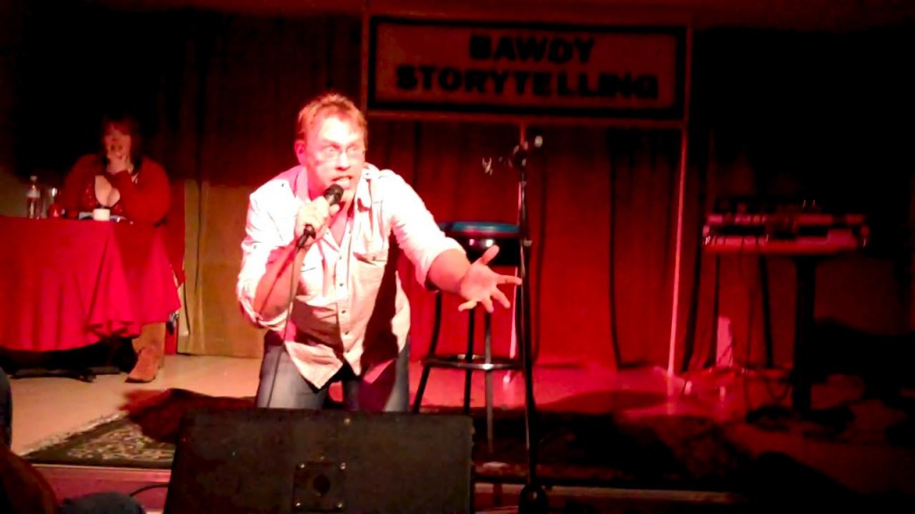 Reid Mihalko on his knees begging the audience while he tells a story about meeting swingers at a resort in Jamica