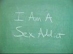 The phrase "I am a sex addict" written on a chalk board in chalk