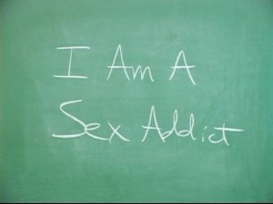 The phrase "I am a sex addict" written on a chalk board in chalk