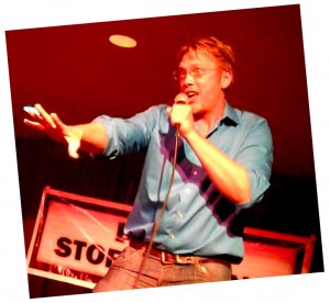 Sex and relationship expert Reid Mihalko wearing a blue shirt annimatedly telling story on stage at a Bawdy Storytelling event