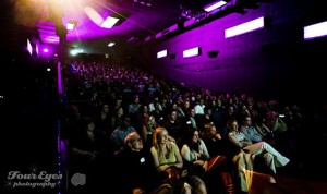 Entertained adults packed into an auditorium with purple lighting
