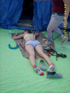 An exhausted Camp Beaverton woman asleep in front of the Beaver Den at Burning Man with a dildo balanced on her butt and several others strewn around her