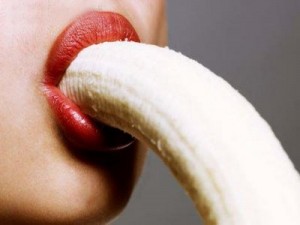 A woman's mouth with a peeled banana entering it