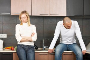 A heterosexual couple not speaking to one another during an argument while wearing matching white turtlenecks sitting in a modern kitchen