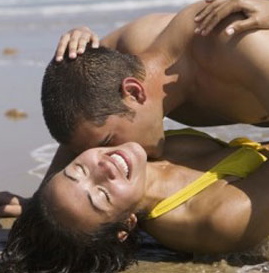 Happy, interracial couple laughing and kissing in the surf on the beach