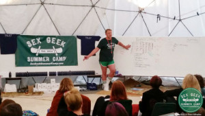 Sex and relationship educator Reid Mihalko teaching in a geodesic dome in front of dry erase boards and an audience at Sex Geek Summer Camp in 2014