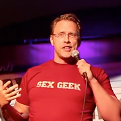 Sex and relationship expert Reid Mihalko of ReidAboutSex.com wearing one of his Sex Geek tshirts and speaking into a mic
