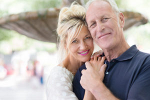 Attractive romantic middle-aged couple posing for their portrait with the heads close together and clasped hands in front of a fountain