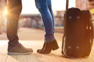 Closeup shot of woman feet standing on tiptoe while embracing her man at railway platform for a farewell before train departure. A travelling luggage is on the foreground.