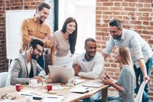 Group of cheerful young people discussing something with smile and gesturing while leaning to the table in office