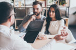 They need expert advice. Young couple sitting together at the desk and listening to their financial advisor