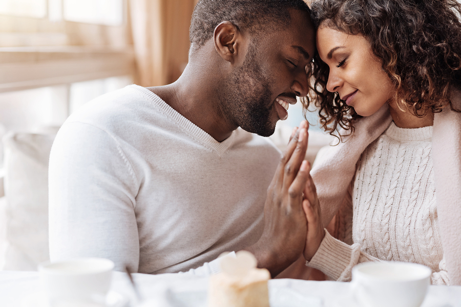 Peacefulness in us. Delighted peaceful positive African American couple sitting in the cafe and touching hands of each other while expressing peacefulness and love