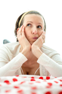 White woman wearing a white sweater thinking while laying on a red polkadot blanket