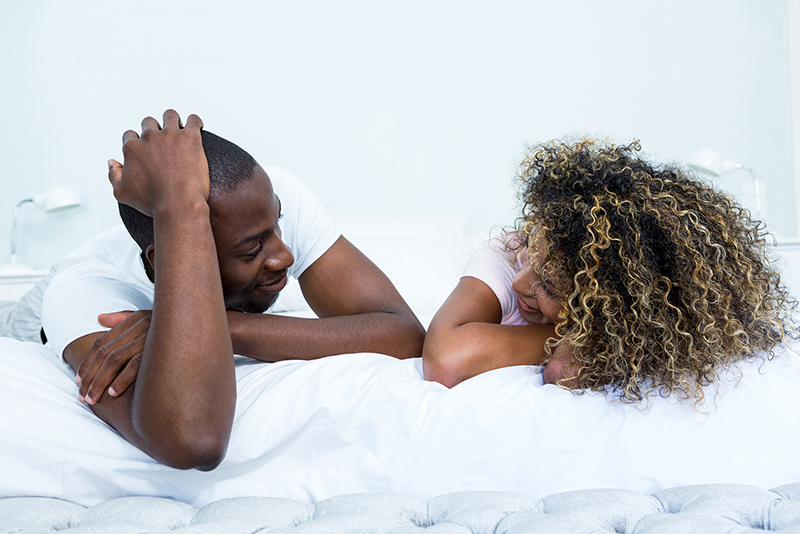 Young POC couple lying on bed and happily talking to each other