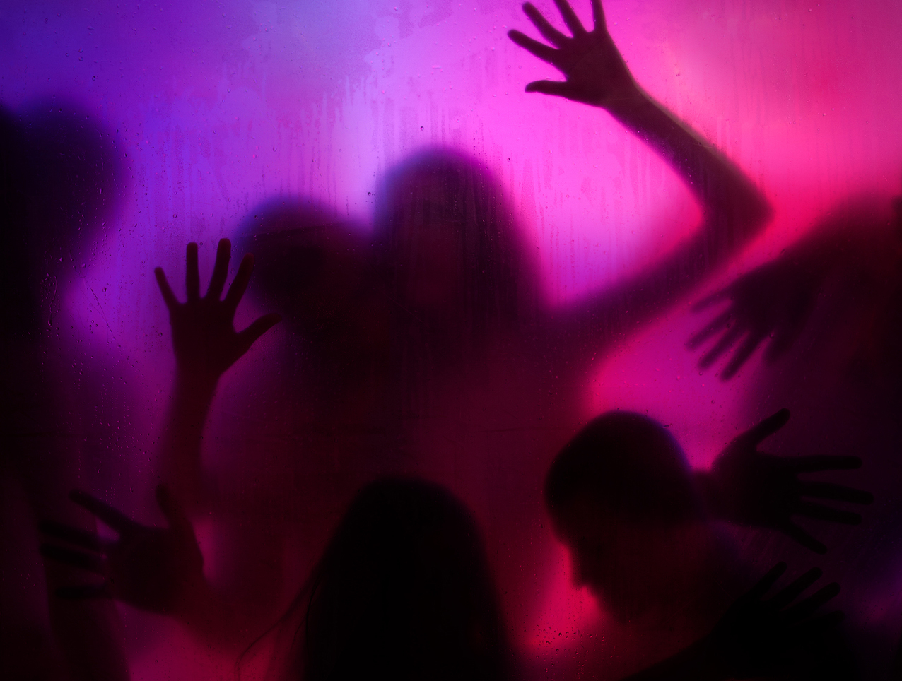 Group of naked people in silhouette behind frosted, translucent glass lit with purple and pink lights engaging in sexual activity