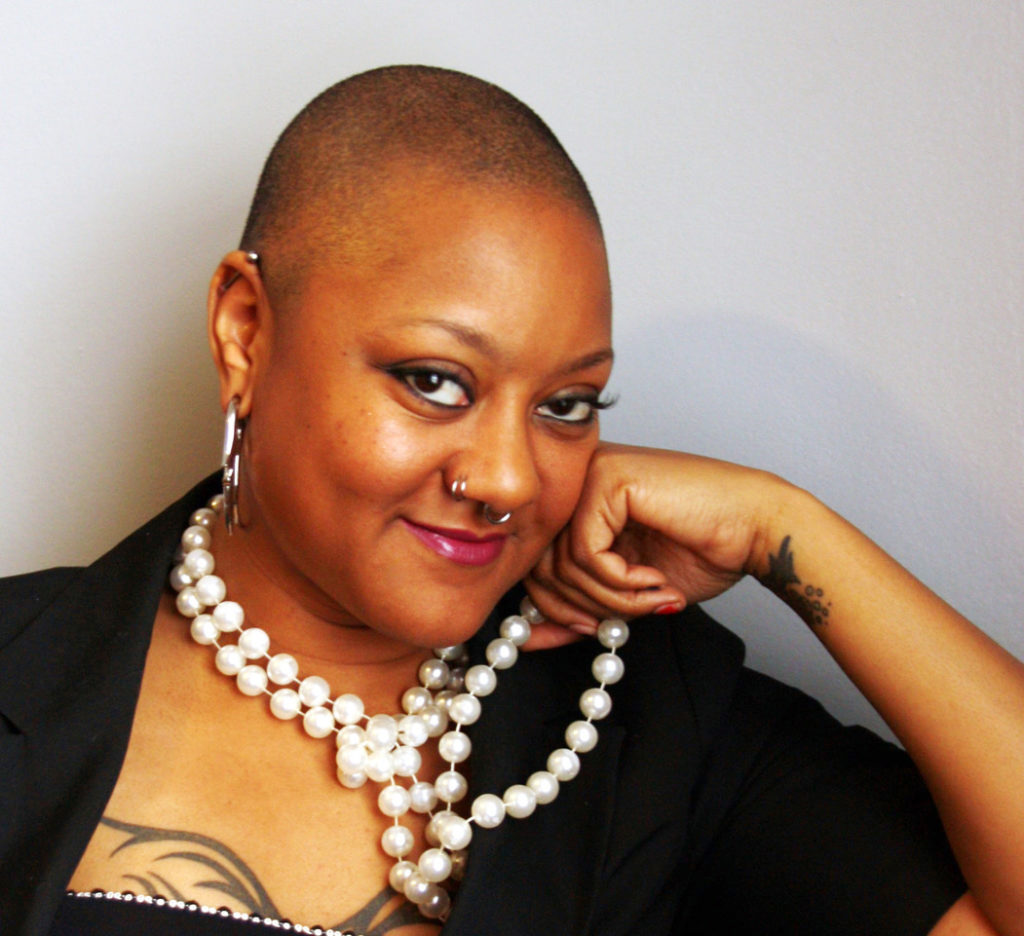 Photo a beautiful black woman with a shaved head and a playful smirk (Marla Renee Stewart) wearing pearls and a dark top