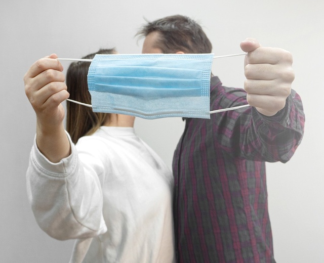 Mature white couple kiss while takes off protective medical mask and obscuring their faces with the mask out in front of them