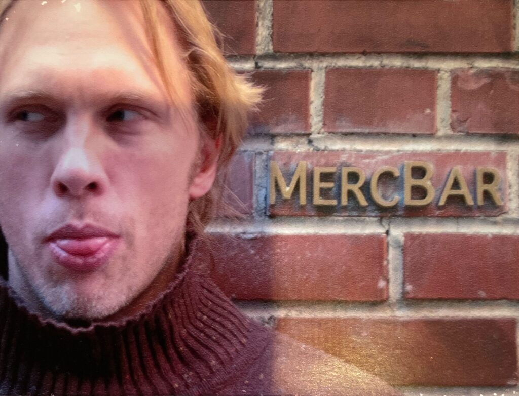 Image of Reid in 2004 standing next to the sign for New York City's famous and now defunct MercBar