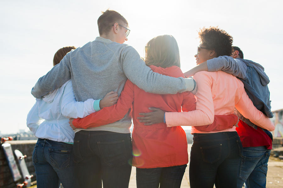 Group hug of 5 adults with their arms around each other looking off into the sunny sky