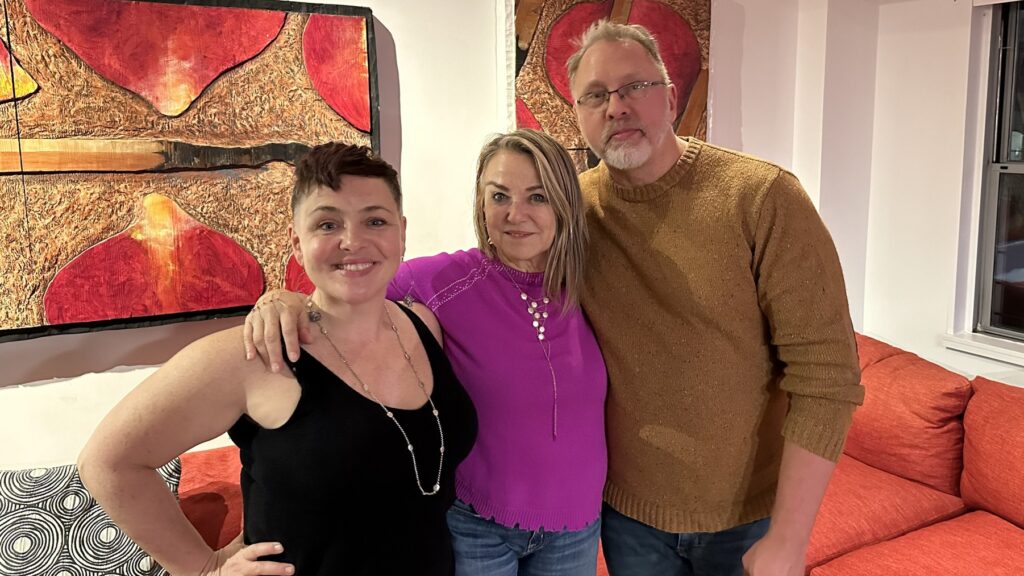 Diana Adams, Esther Perel, and Reid Mihalko stand next to one another with arms arounds the others shoulder while smiling at the camera.