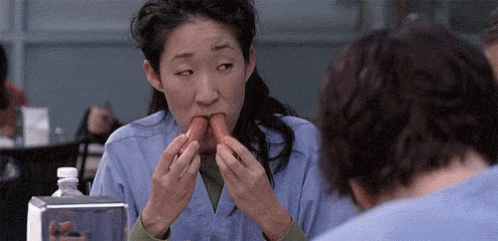 GIF of Asian actor Sandra Oh (Cristina Yang on Grey's Anatomy) eating two hot dogs as once 