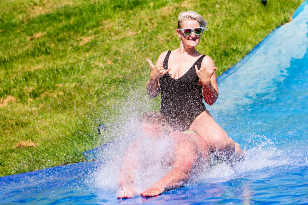 Blond woman riding a man (Reid) down a massive blue water slip 'n slide