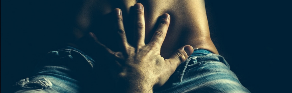 Image of a white man's open hand seductively and gently caressing a woman's tummy who's wearing unbuttoned, faded bluejeans 